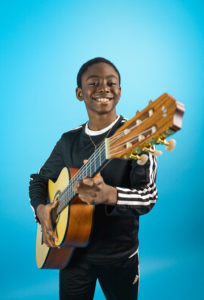 Guitar student smiles while holding guitar and looking at the camera